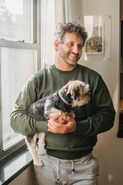 A cheerful man holding his Yorkshire Terrier in a sunlit room, embodying warmth and companionship.